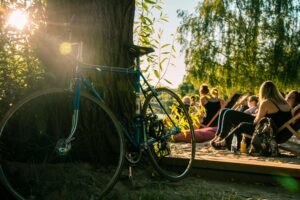 Bicycle leaning against tree in sunny park, friends lounging nearby in summer.
