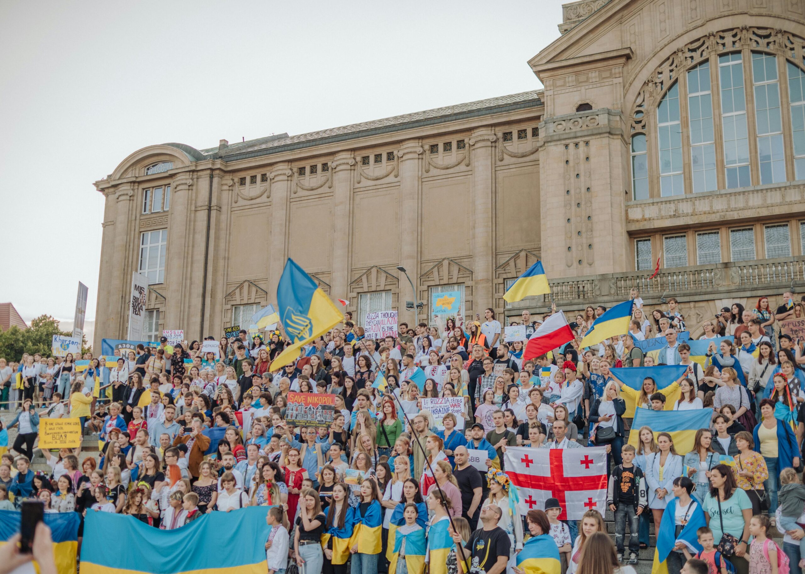 A vibrant crowd gathers in Szczecin, Poland for a public demonstration waving various national flags.