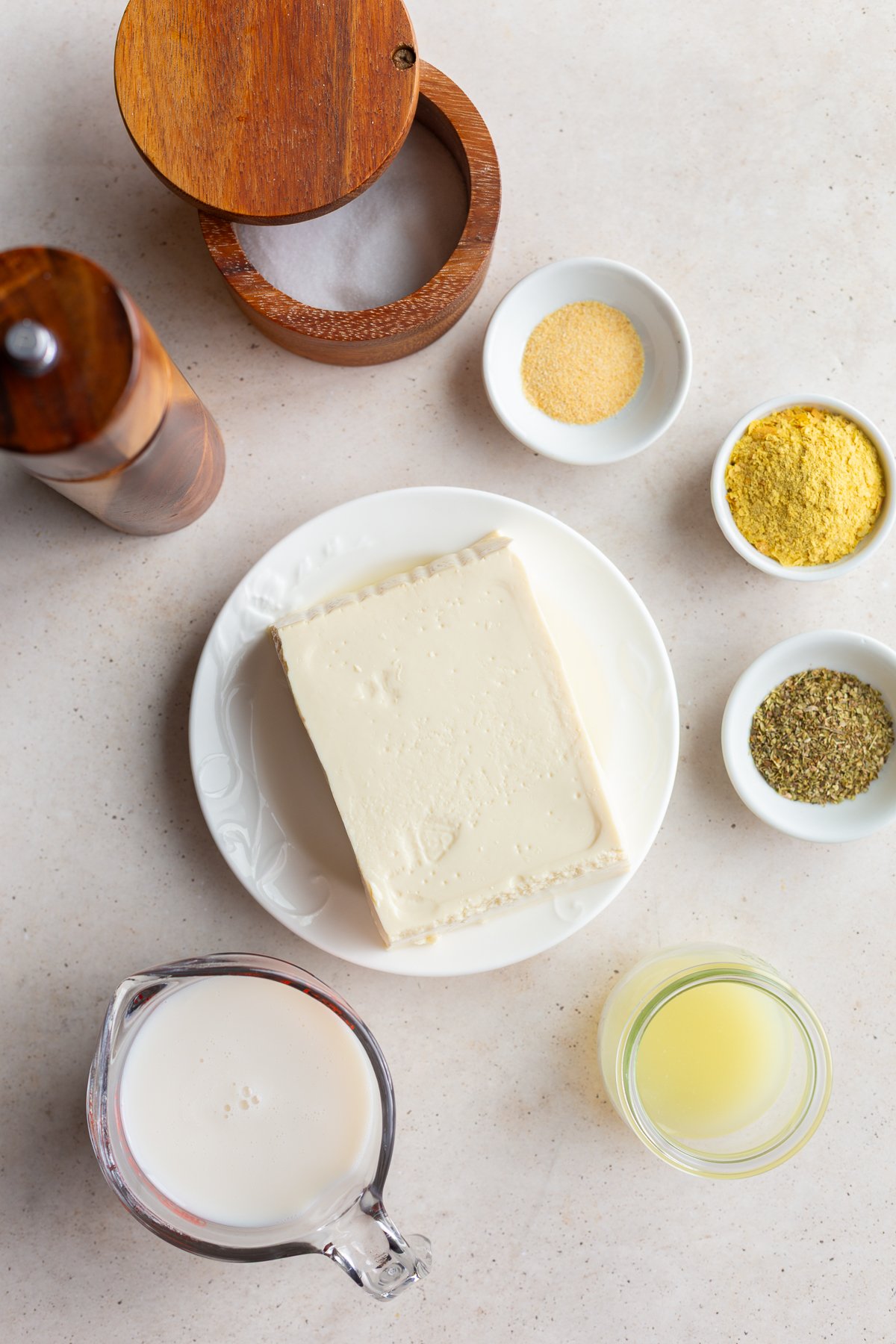 Tofu on a plate near small bowls of seasonings and a glass of milk.