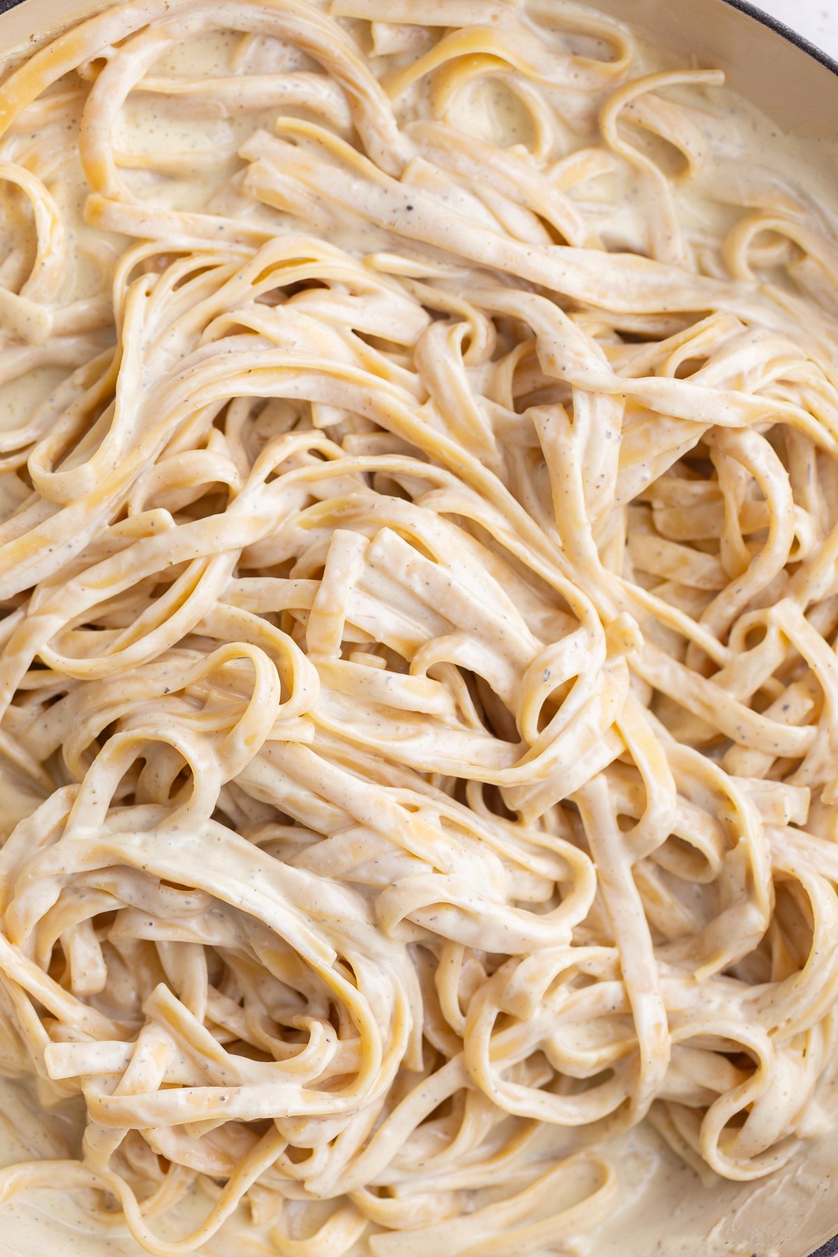 White creamy sauce tossed with pasta in a pot.