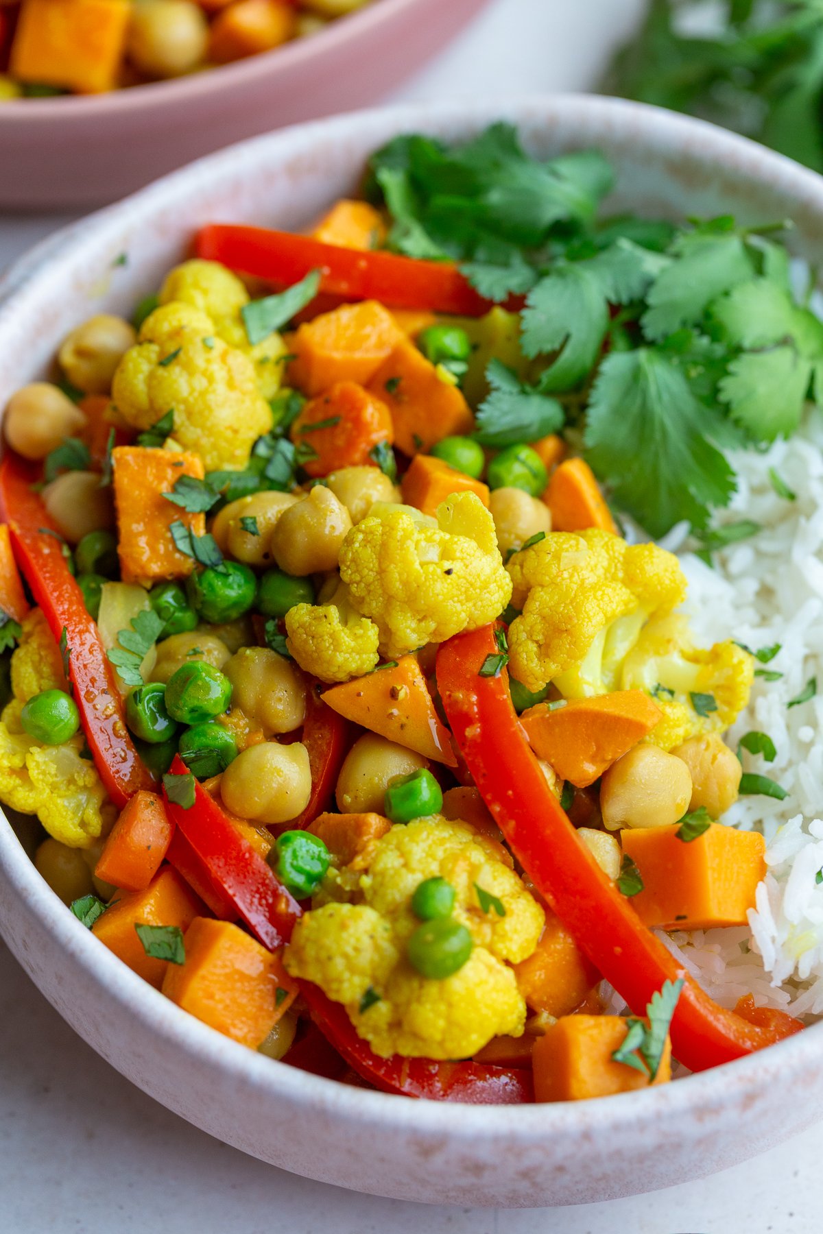 chickpea and sweet potato curry in a bowl that also has red pepper and peas in in served on white rice with cilantro on the side