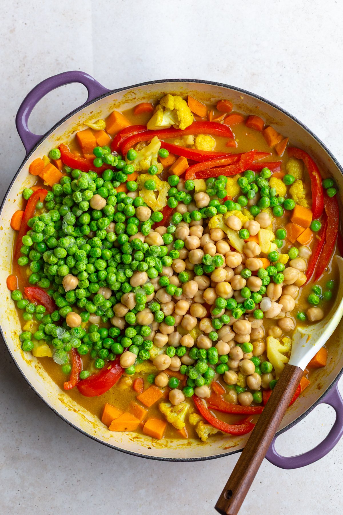 HOW TO MAKE A SWEET POTATO CURRY: veggies in a skillet with a curry sauce. Chickpeas and peas have been added on top but not stirred in yet