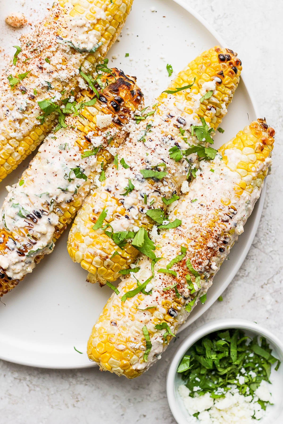 mexican street corn on the cobb on a white plate topped with cilantro and cotija